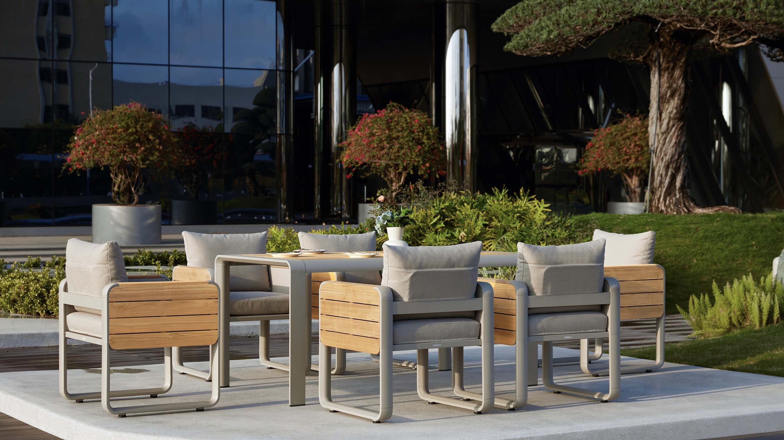 Ensemble repas extérieur haut de gamme en aluminium et teck FSC avec coussins, design moderne aux courbes élégantes.