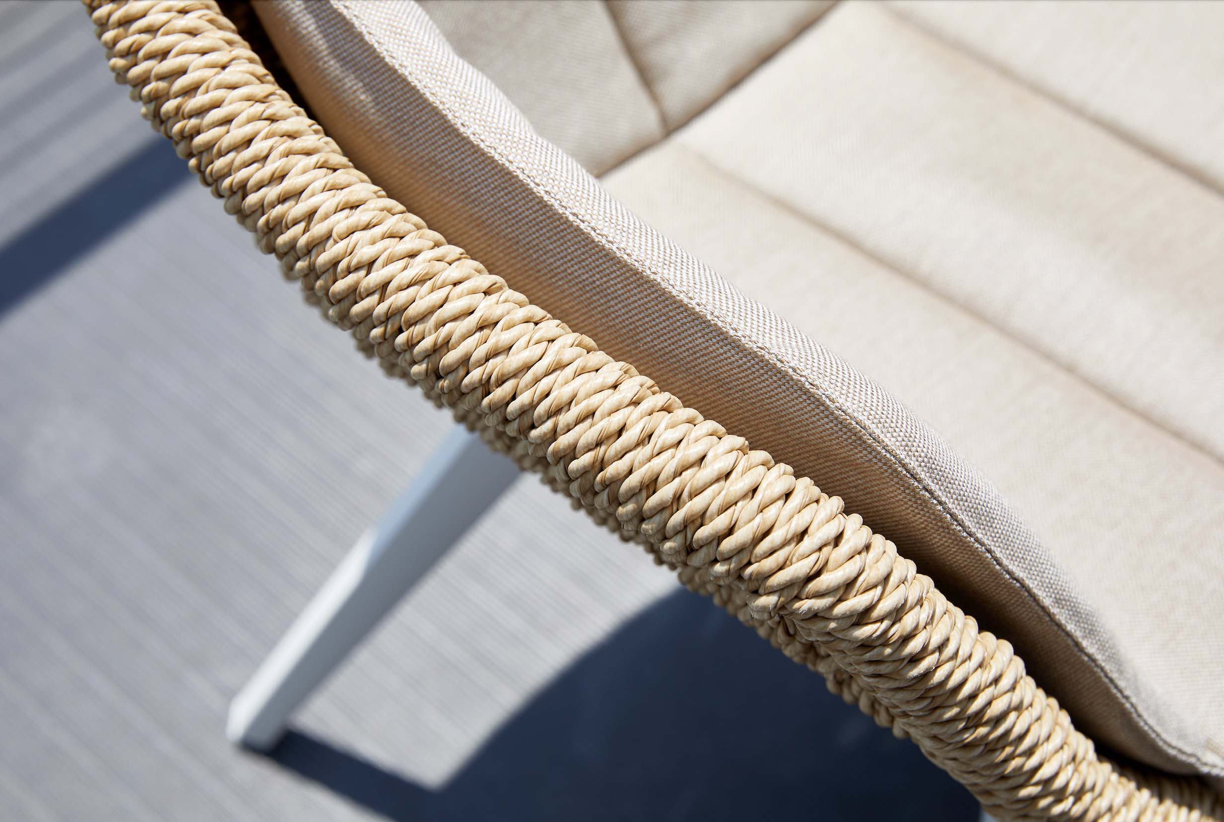 Détail d'un fauteuil repas de jardin en aluminium haut de gamme avec résine tressée beige, coussin crème épais, finition.