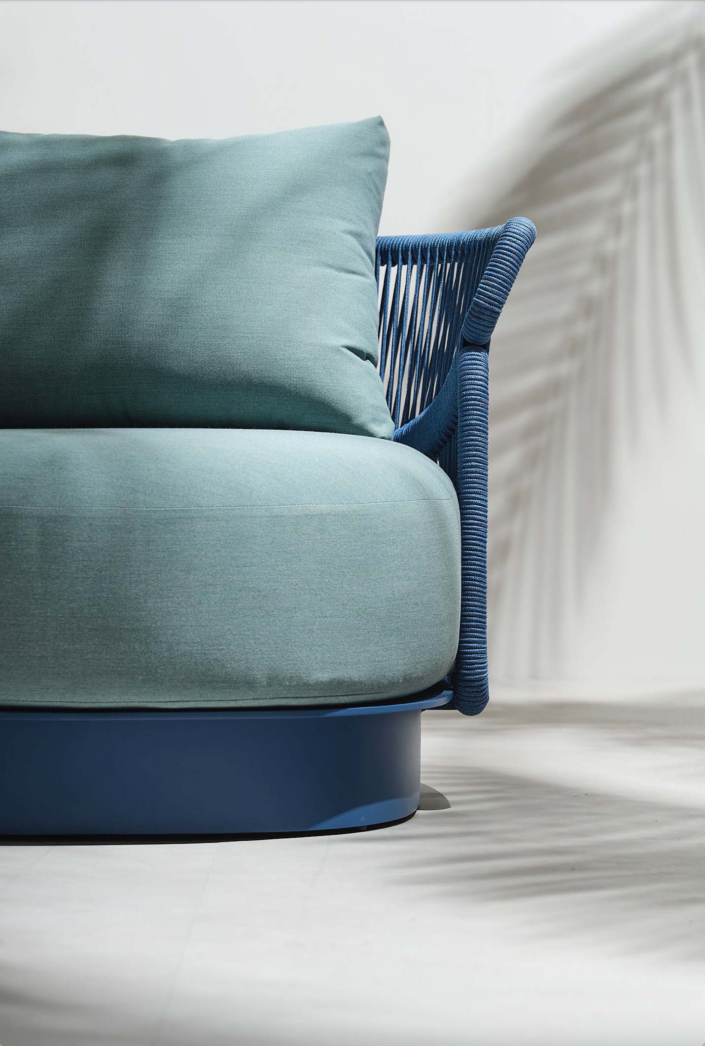 Fauteuil de jardin luxueux bleu en corde tressée et aluminium avec coussins verts, design italien haut de gamme, ambiance.