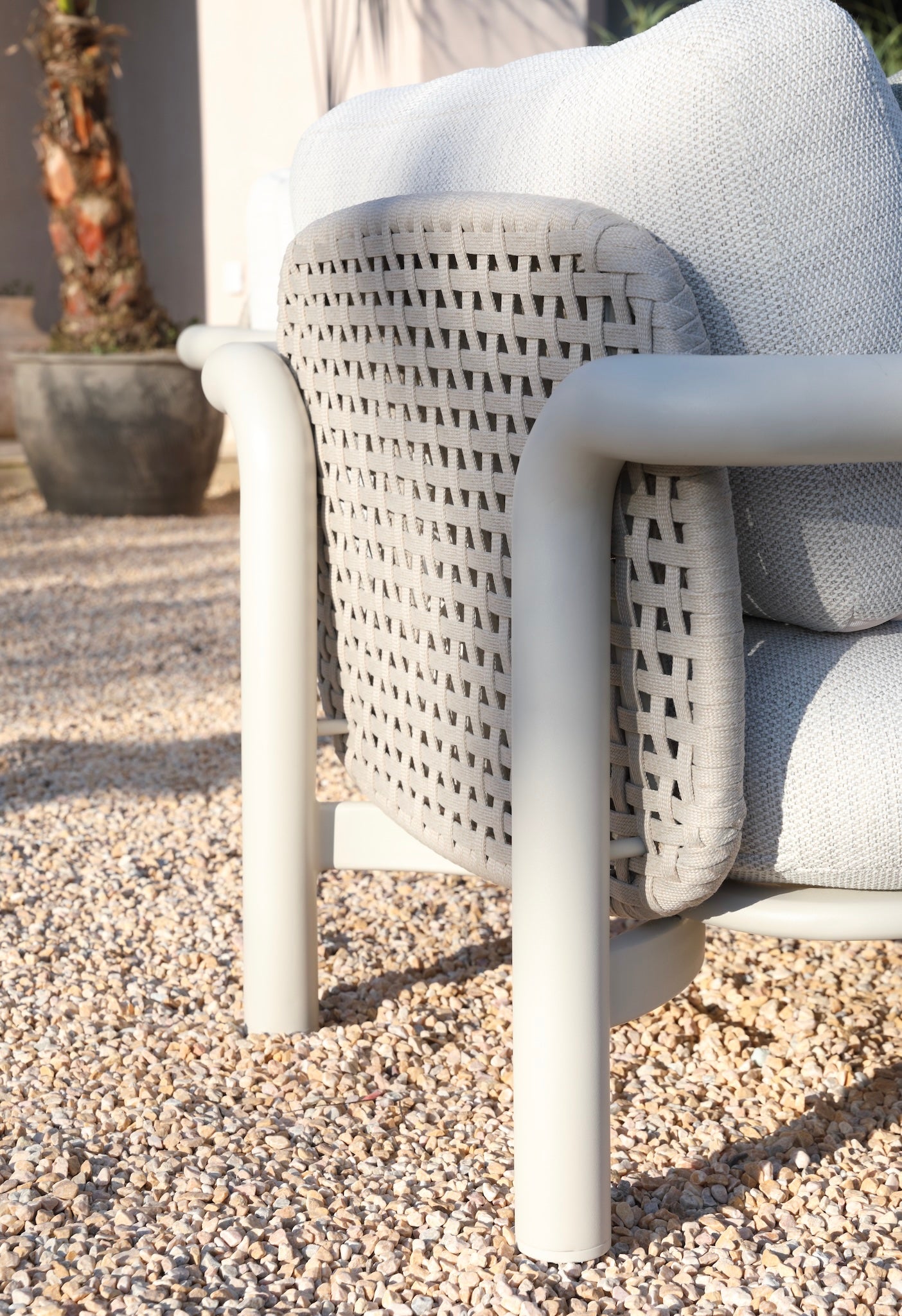 Fauteuil d'extérieur au design luxe avec structure cylindrique en aluminium, dossier en corde tressée gris clair, coussins.