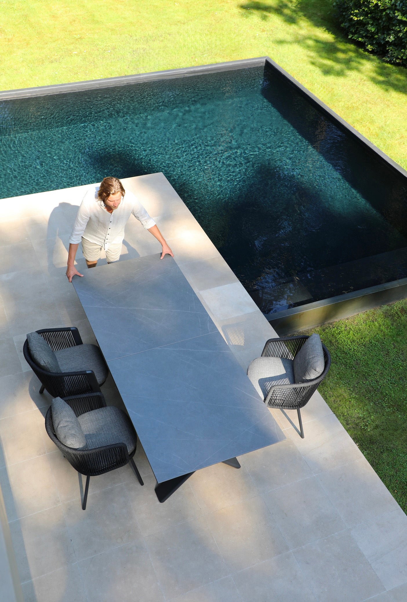 Fauteuils repas d'extérieur en aluminium haut de gamme inoxydable avec assise en corde noire, autour d'une table extensible.