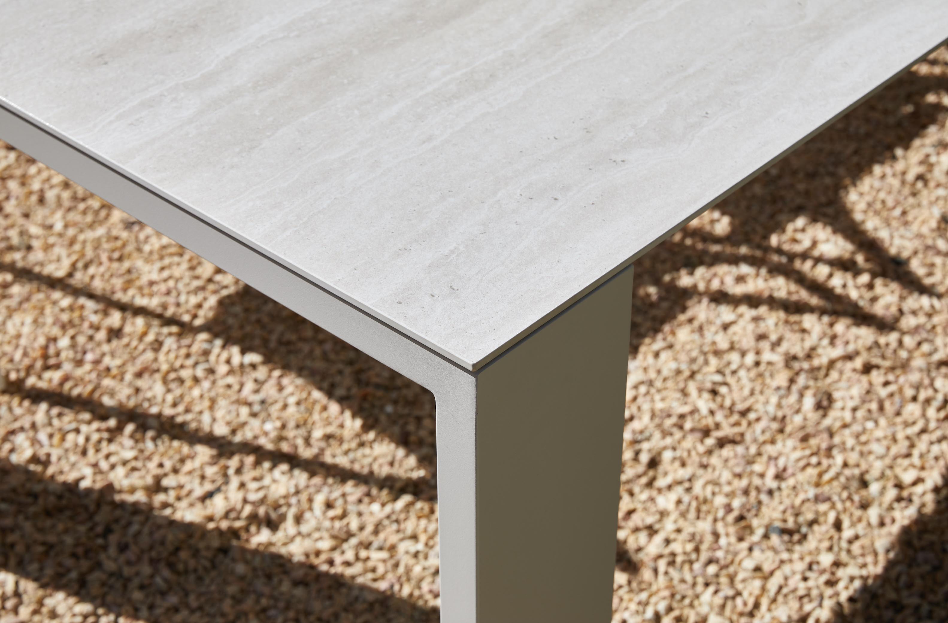 Table d'extérieur avec plateau en céramique blanc effet pierre, pieds en aluminium haut de gamme inoxydable beige clair.