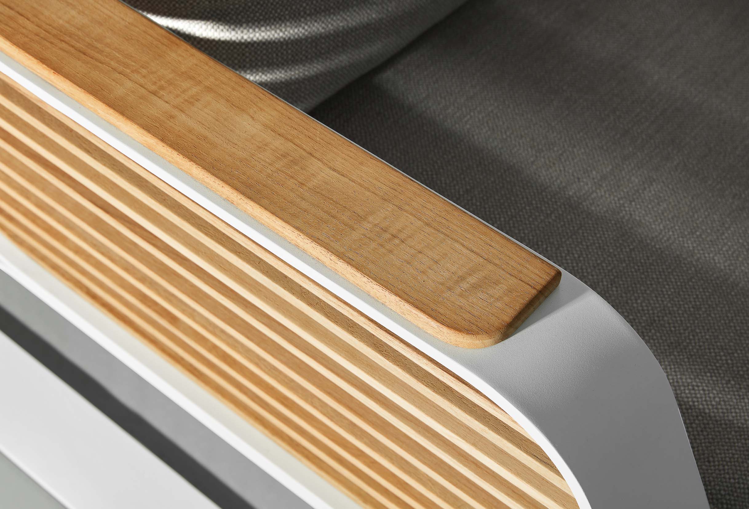 Détail d’un accoudoir en aluminium blanc laqué et Teck FSC aux lignes architecturales, coussin gris clair luxueux avec.