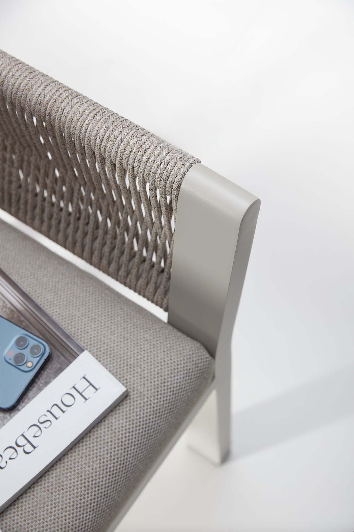 Détail d’un coin de chaise d’extérieur en aluminium gris clair, dossier en corde tressée beige, assise avec coussin.