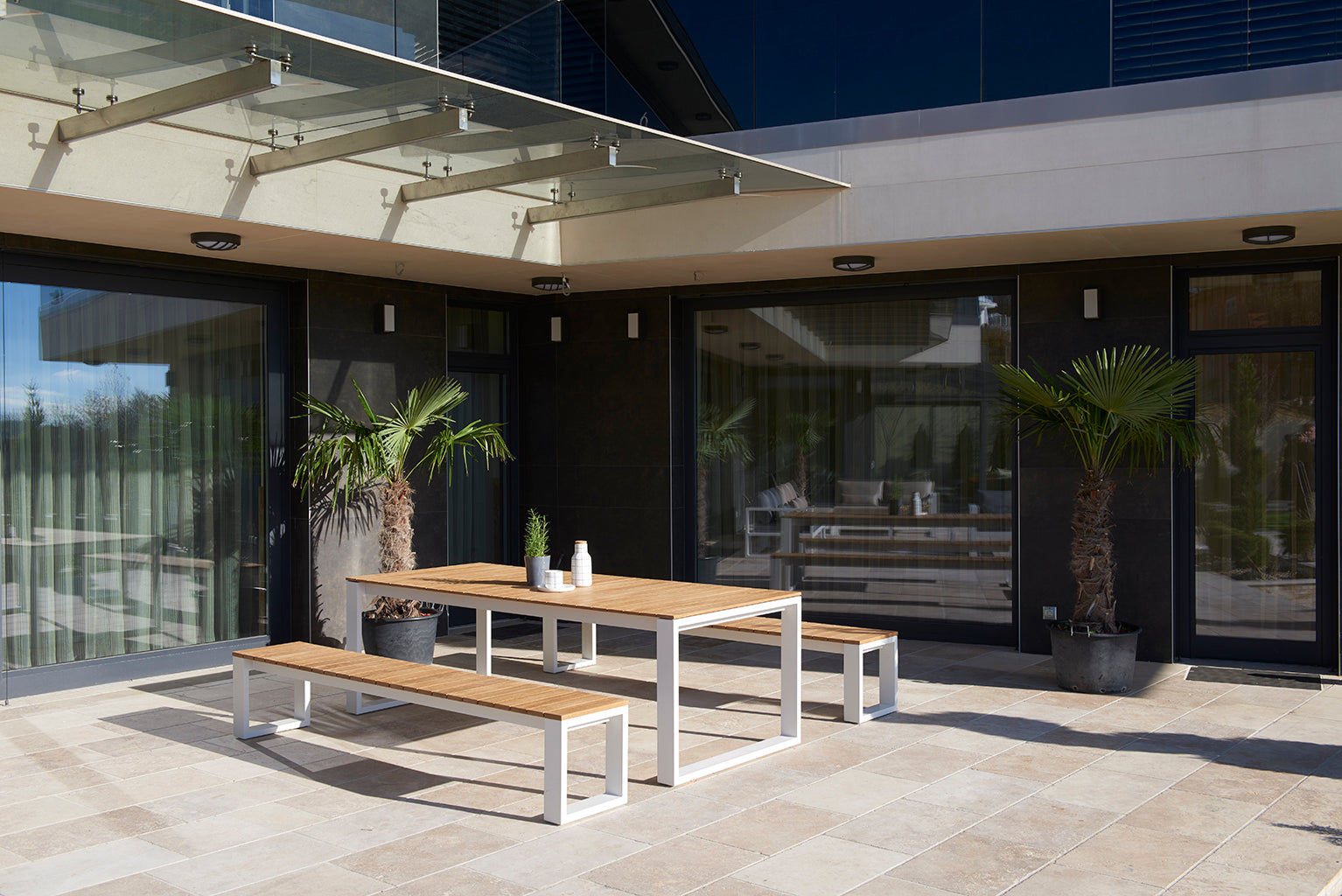 Table de jardin COMO 200cm en teck FSC avec cadre en aluminium haut de gamme, associée à des bancs au design épuré, élégance. 