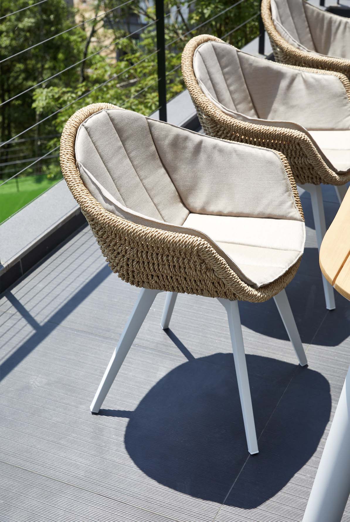 Fauteuil repas en résine tressée beige avec coussin crème, structure en aluminium haut de gamme blanc mat, pieds élancés.