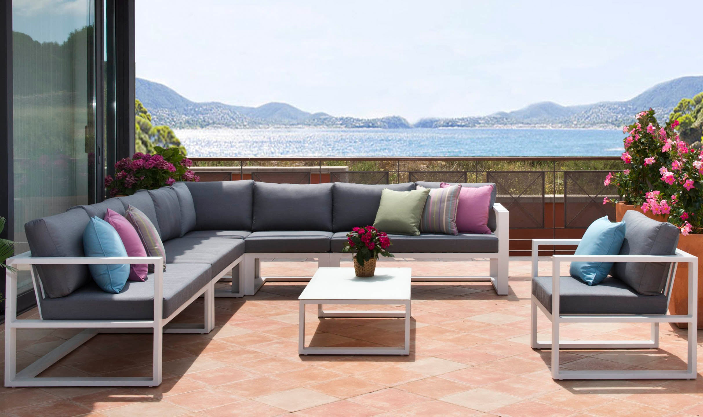 Salon de jardin modulable haut de gamme en aluminium blanc, coussins gris et colorés, table basse carrée blanche, ambiance.