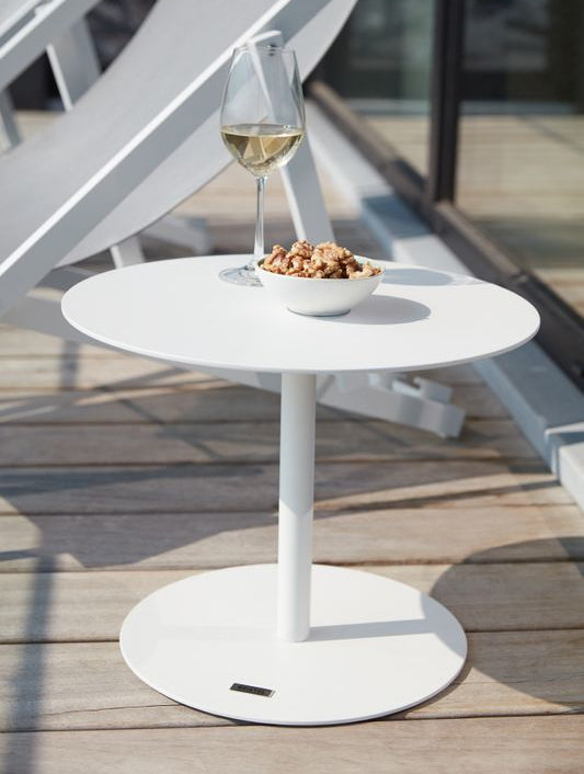 Table basse ronde blanche en aluminium inoxydable avec surface lisse, design épuré et moderne, posée sur terrasse en bois. 